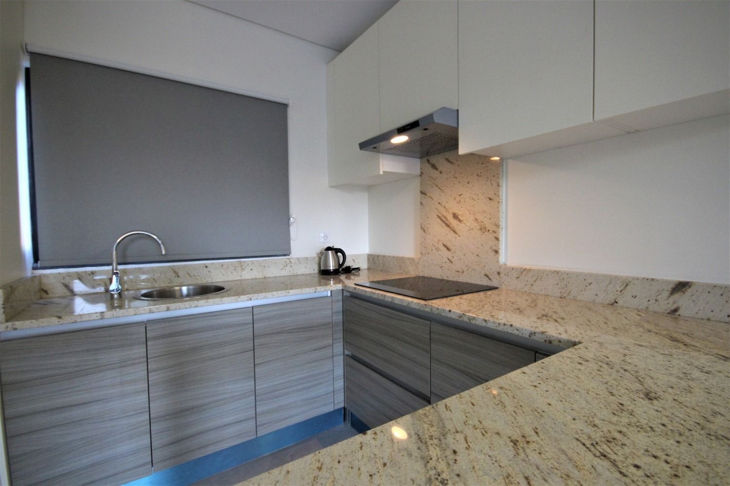 Modern kitchen with light wood cabinets, granite countertops, and a gray window shade.
