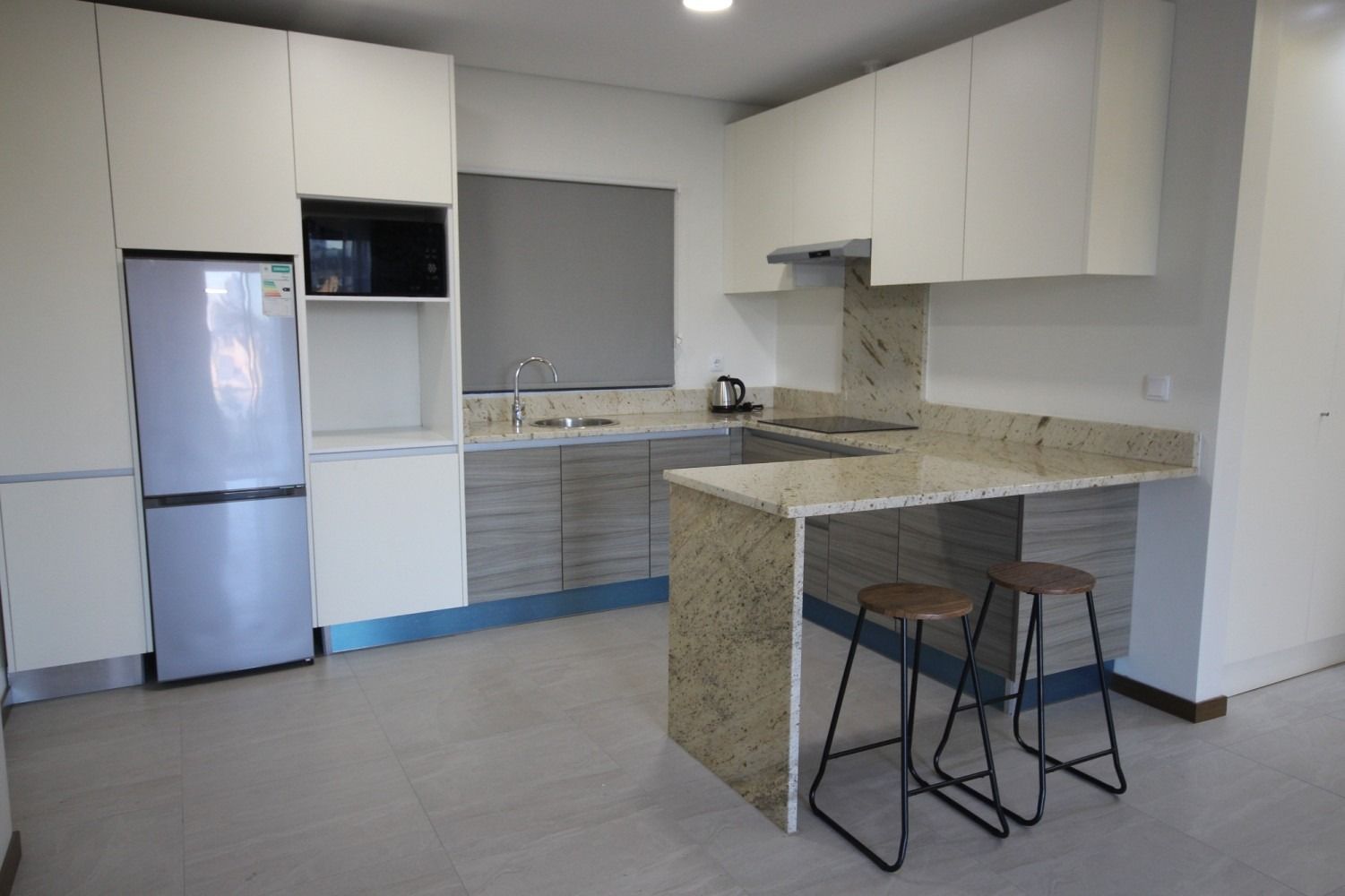 Modern kitchen with white cabinets, stainless steel refrigerator, granite countertops, and breakfast bar with two stools.