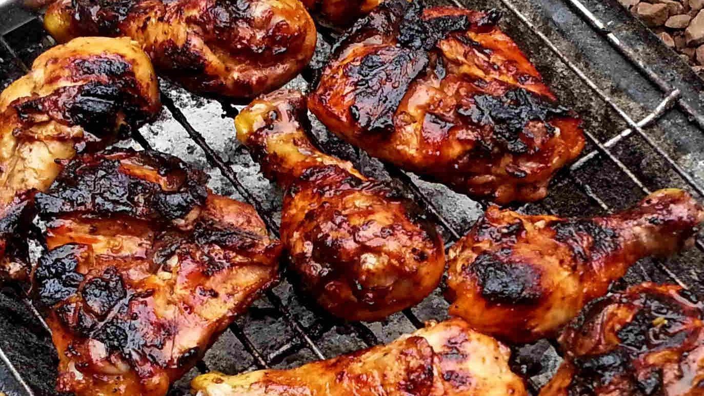 Grilled chicken pieces on a metal grate, with a glossy, charred appearance.