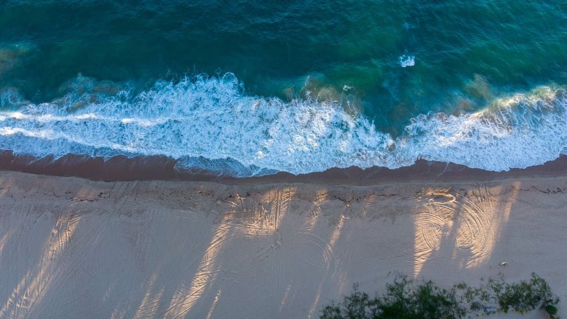 Waves crashing on a sandy beach. Turquoise water, white foam, and shadows cast by sunlight.