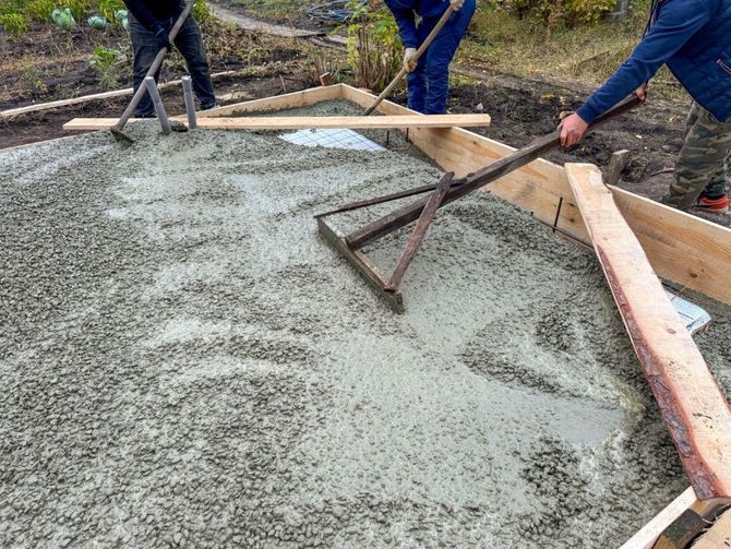 Workers smoothing wet concrete in a foundation form outdoors.