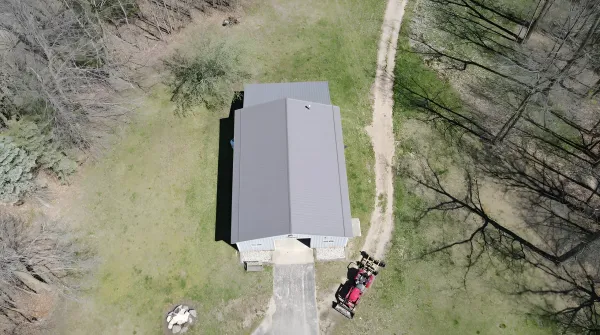 Aerial view of a house with a dark gray roof, driveway, and a red vehicle parked.