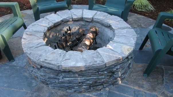 A fire pit is surrounded by green chairs on a patio.