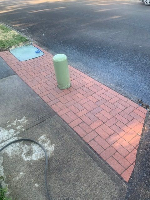 A brick sidewalk with a green pole in the middle of it.