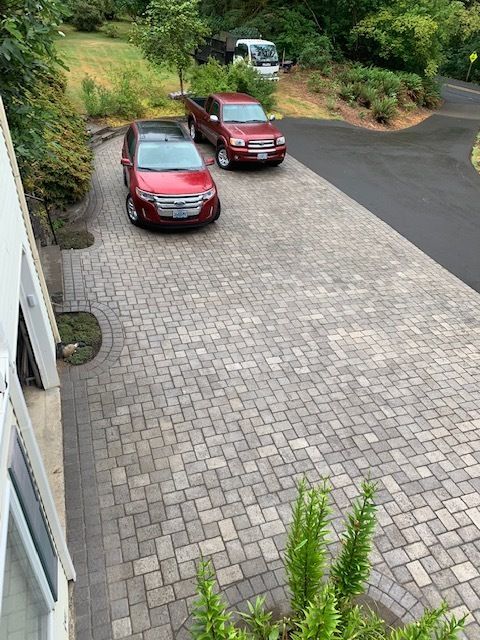 Two red cars are parked in a brick driveway