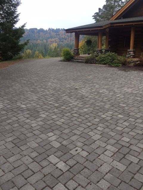 A brick driveway leading to a house with trees in the background