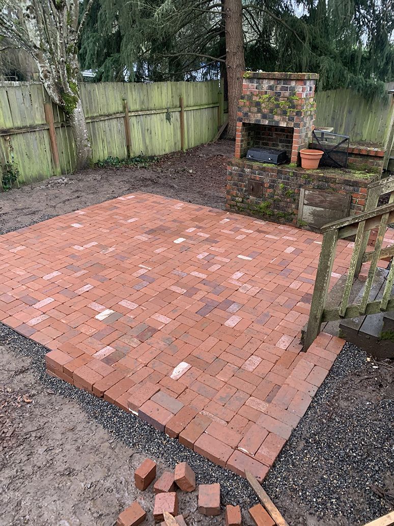 A brick patio is being built in a backyard.