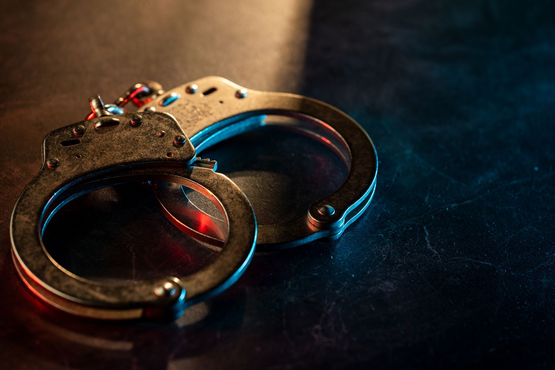 Handcuffs on a dark surface, illuminated by blue and red light.