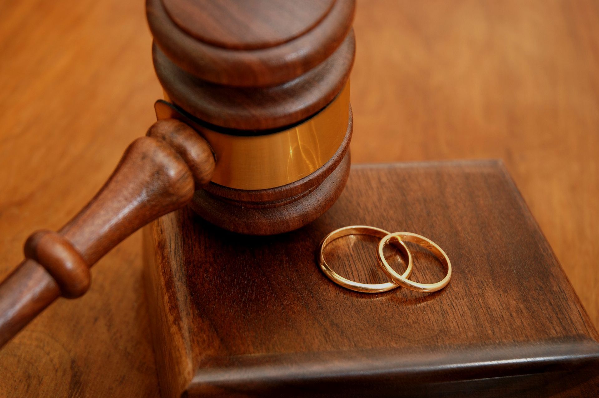 Gavel and block next to two golden wedding rings on a wooden table.