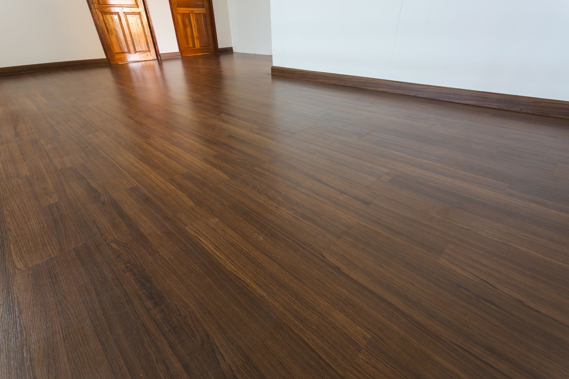 A room with dark wood flooring and white walls, featuring two wooden doors in the background.
