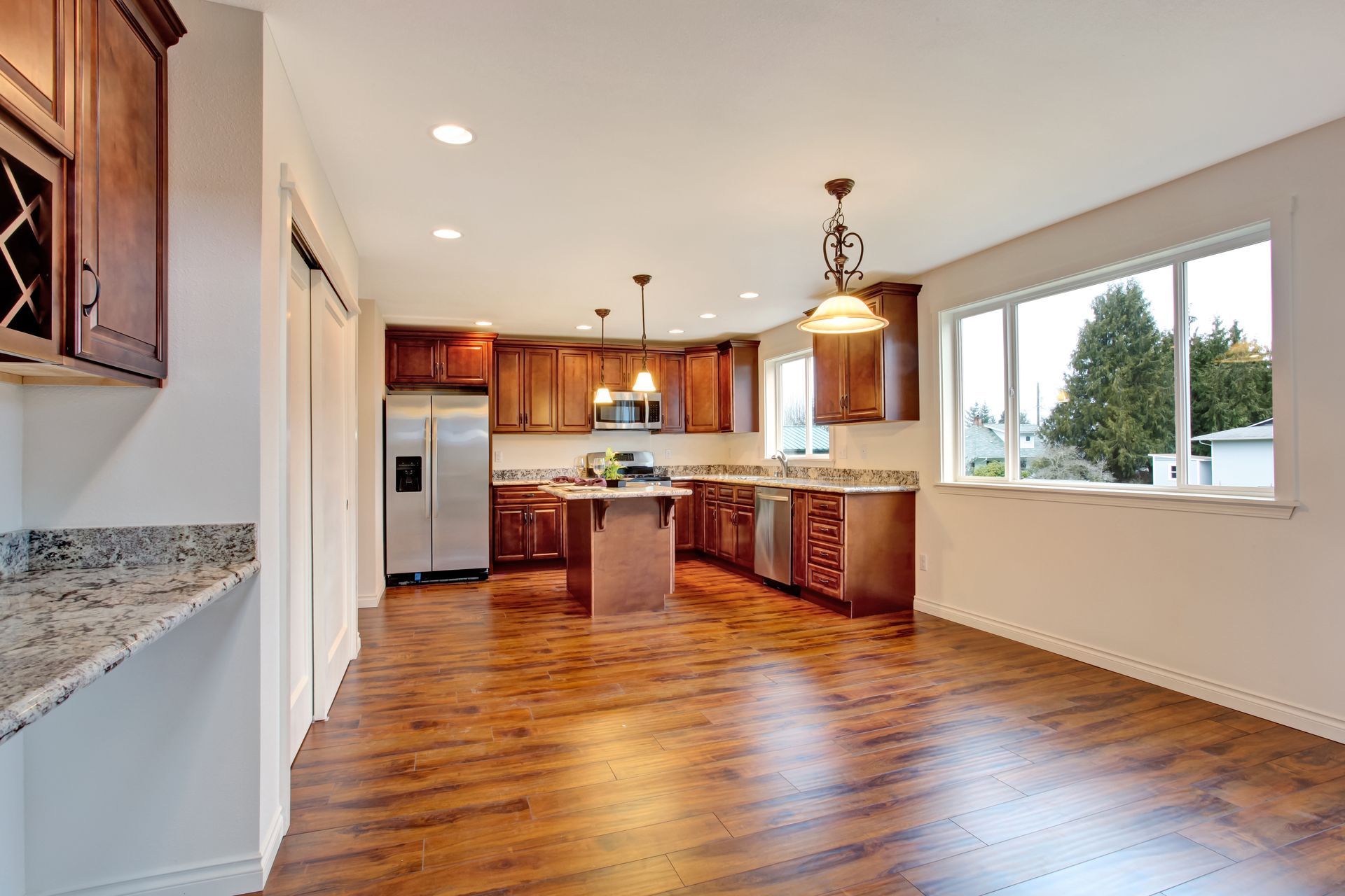 A kitchen featuring wood cabinets, stainless steel appliances, granite countertops, and wood-look flooring.