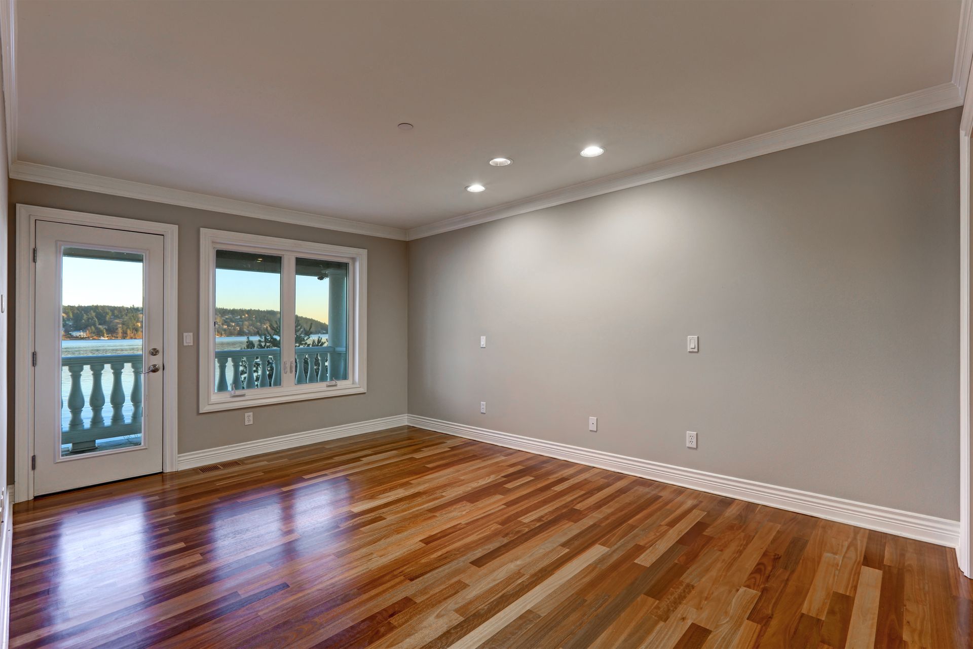 Empty room with warm wood floors, light grey walls, white trim, recessed lighting, and a door leading to a balcony.