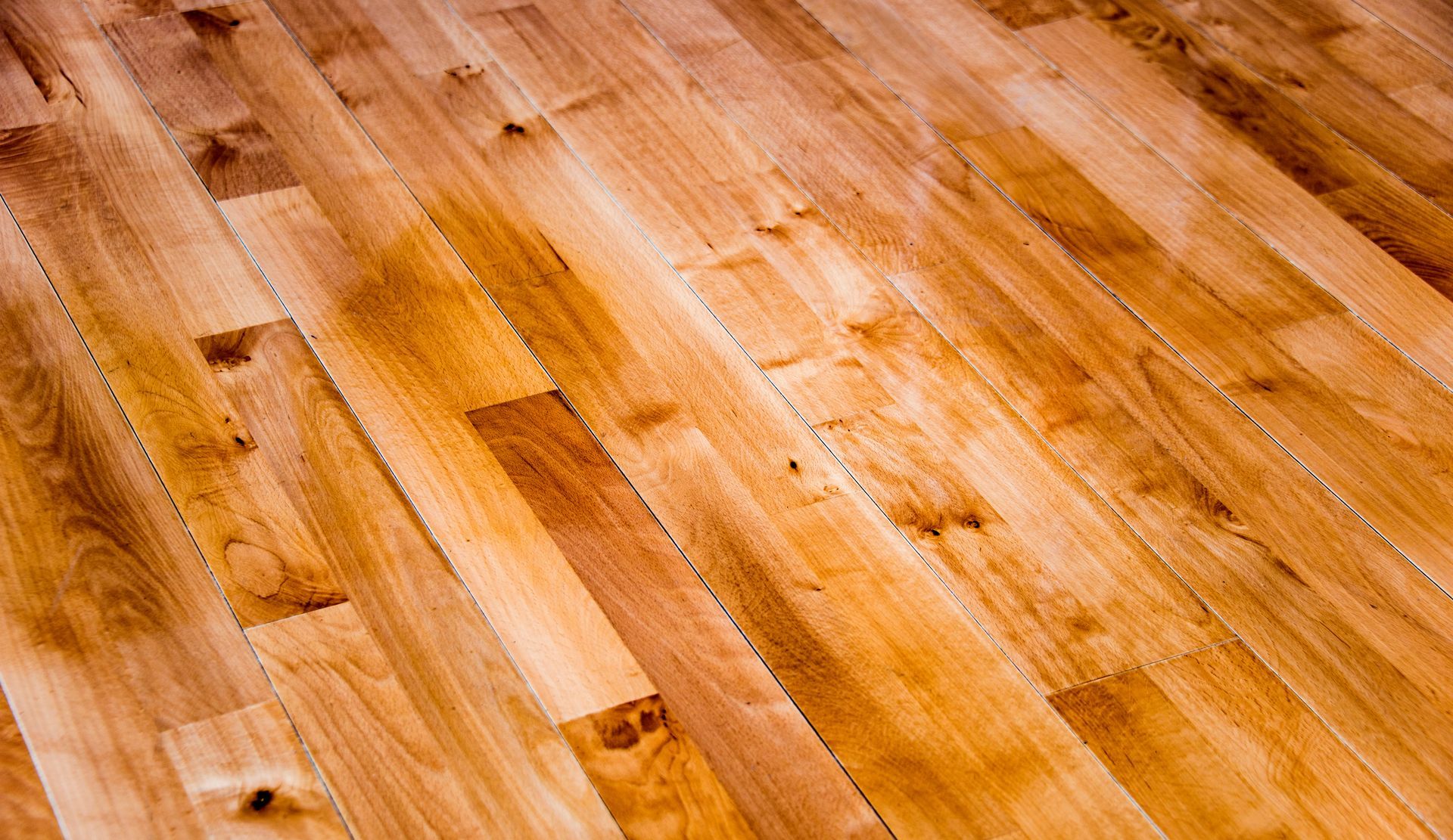 A close-up of polished hardwood flooring showing natural wood grain, knots, and warm amber tones.