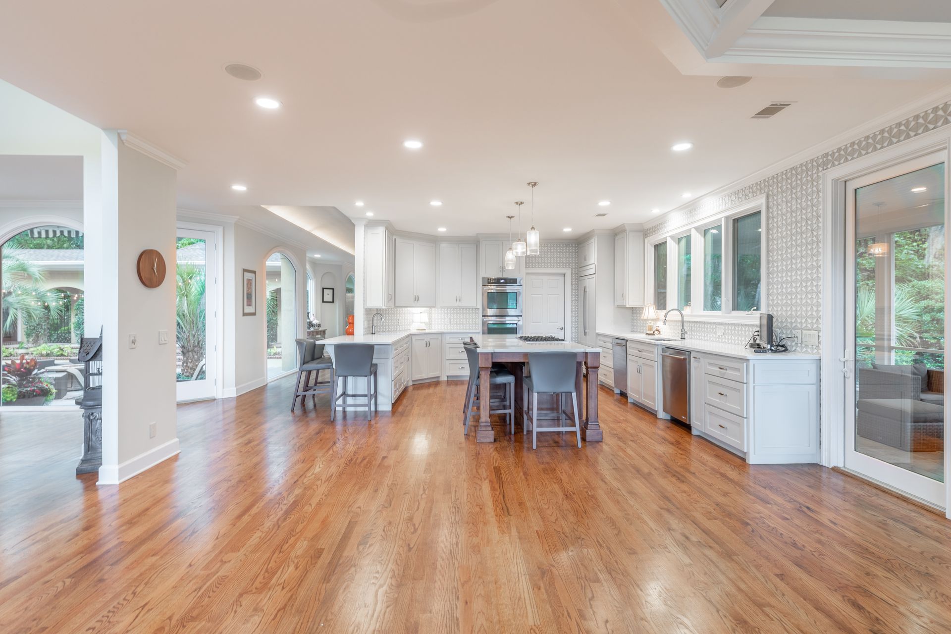 A bright, open-concept kitchen with white cabinets, a central island with bar stools, and polished hardwood flooring.