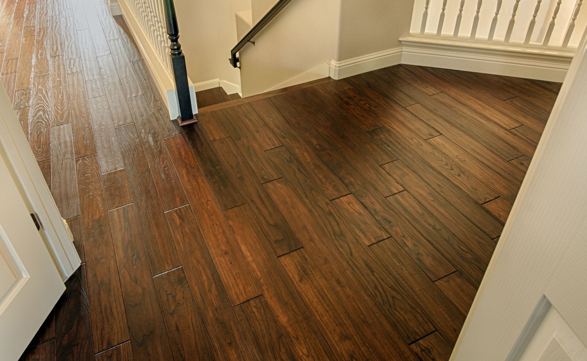 A view from a doorway looking into an interior space with dark wood flooring, a white staircase, and white trim.