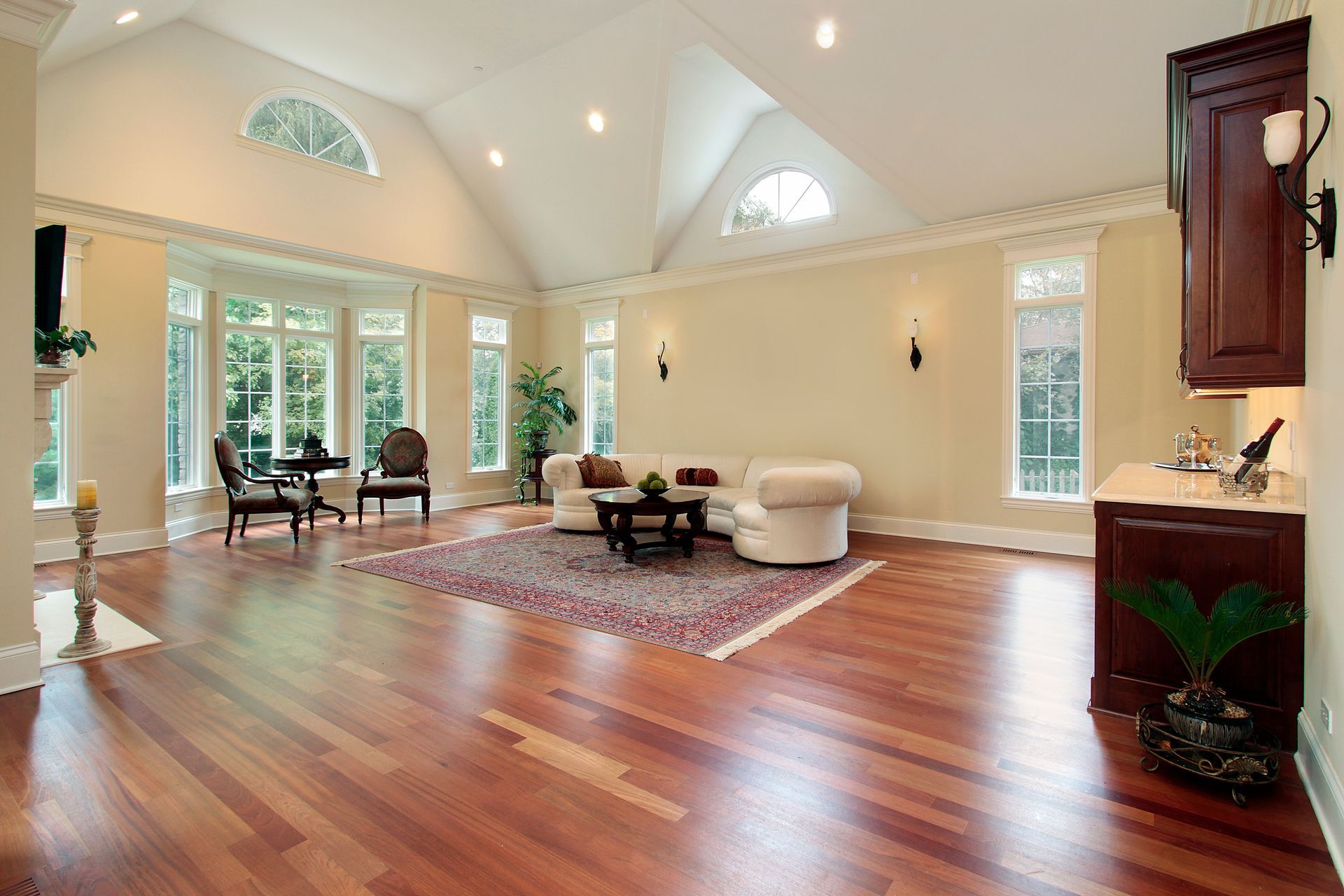 A sunlit living room with high vaulted ceilings, light-colored walls, hardwood floors, a white sofa, and bay windows.