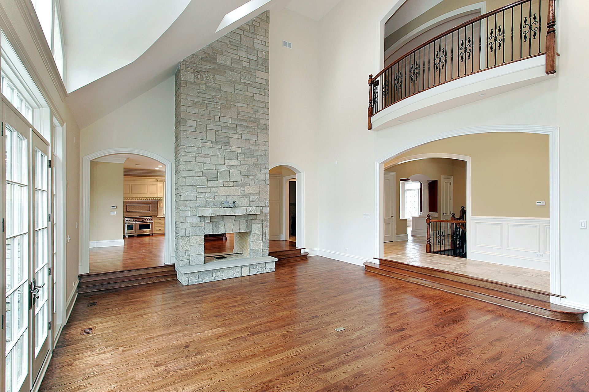 Spacious room with high ceilings, hardwood floors, stone fireplace, and an upper-level balcony overlooking the space.