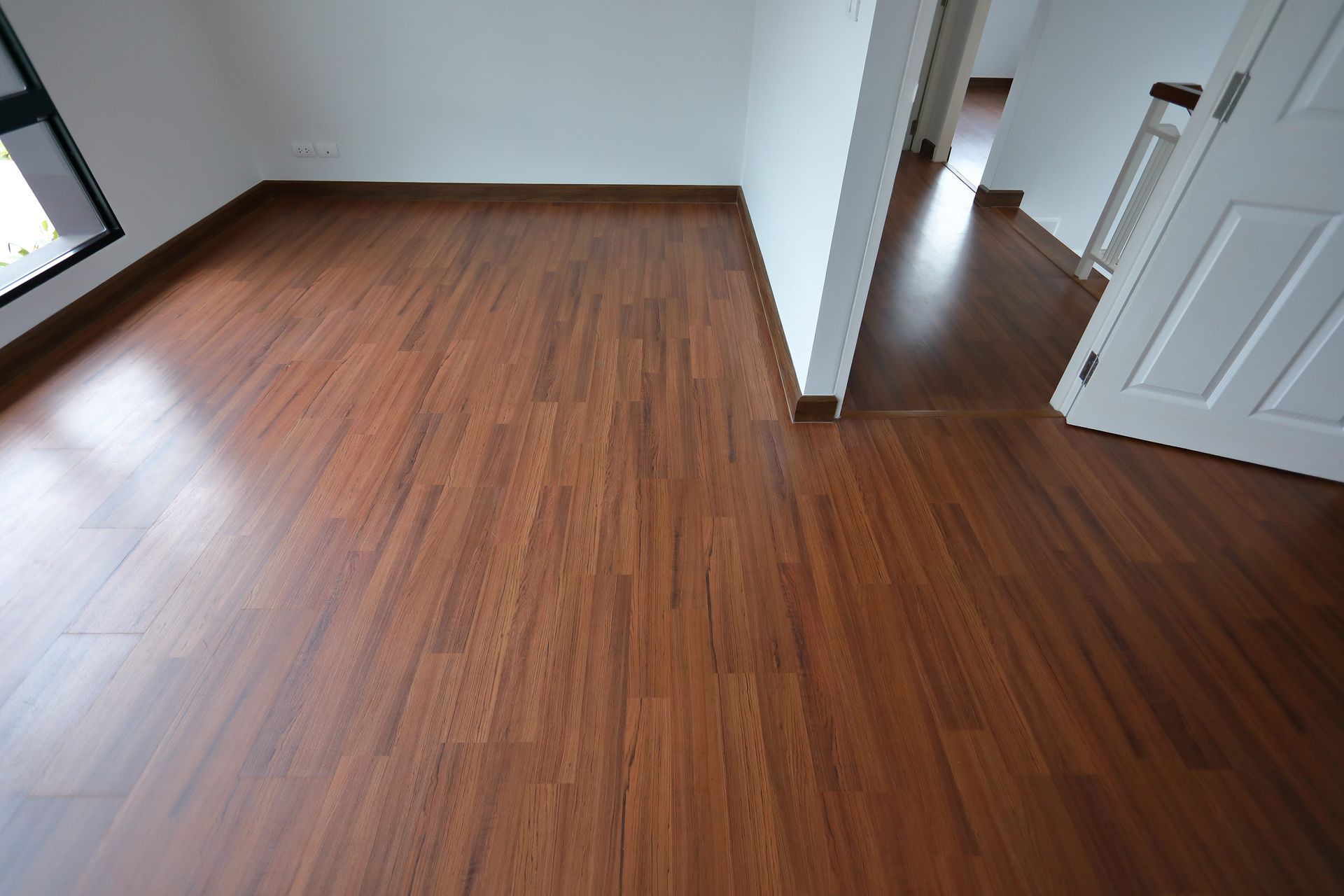 A room featuring warm, wood-grain laminate flooring, white walls, and an open white door leading to a hallway.