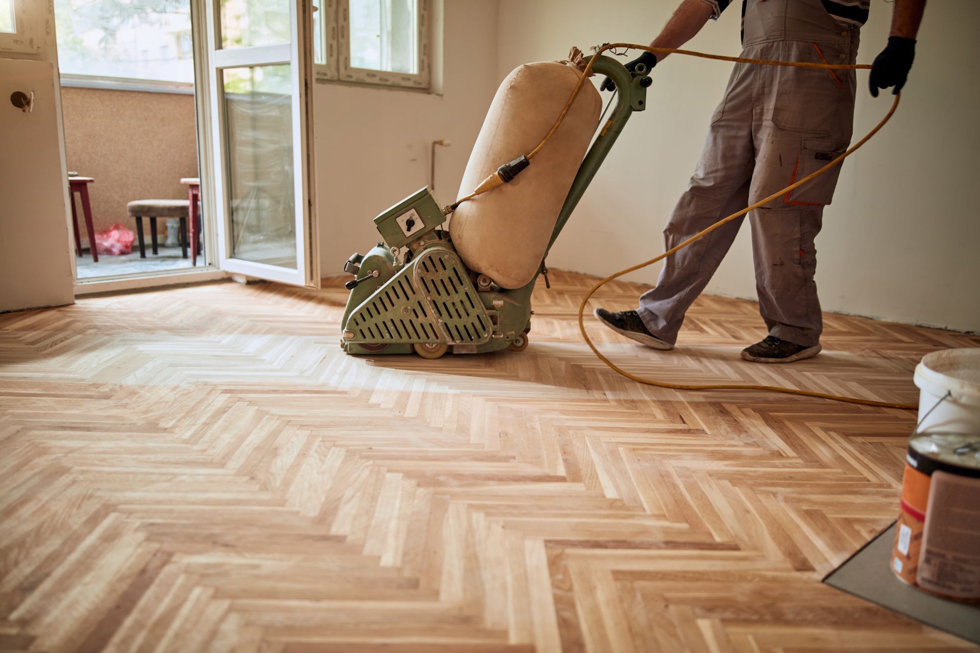 A professional sands a herringbone wood floor with a large industrial machine in a room.