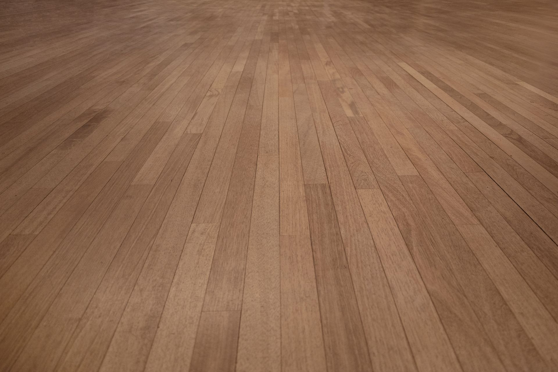 A perspective view of light-brown wooden floorboards with visible grain and seams running toward a center vanishing point.