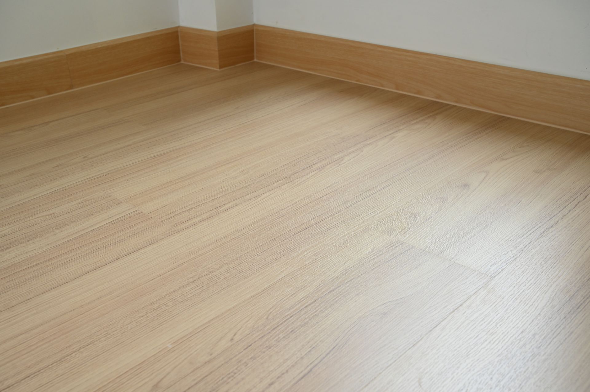 Light-colored wood laminate flooring meets a white wall with matching wooden baseboards.
