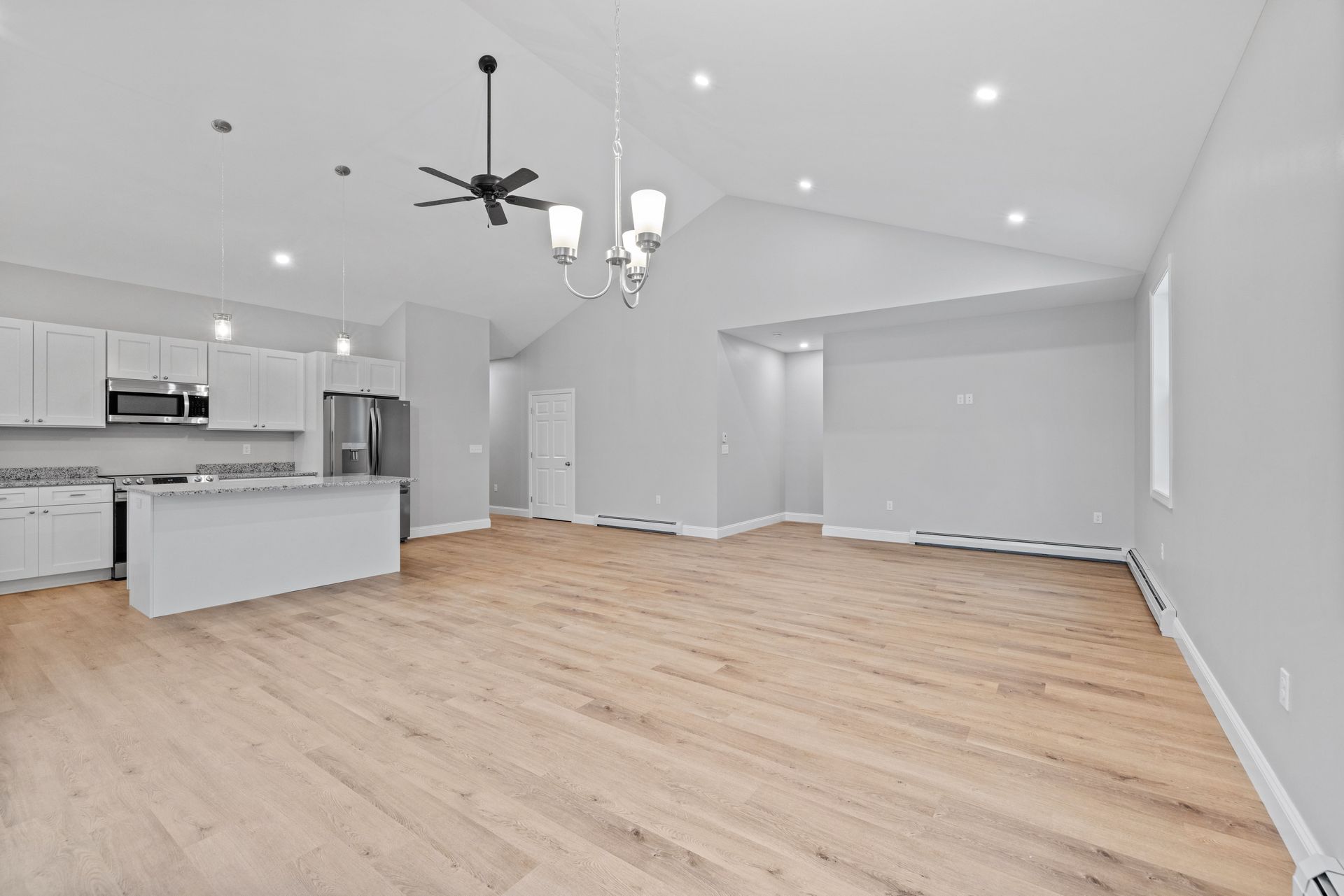 A bright, open-concept kitchen and living area with white cabinets, light wood flooring, and vaulted ceilings.
