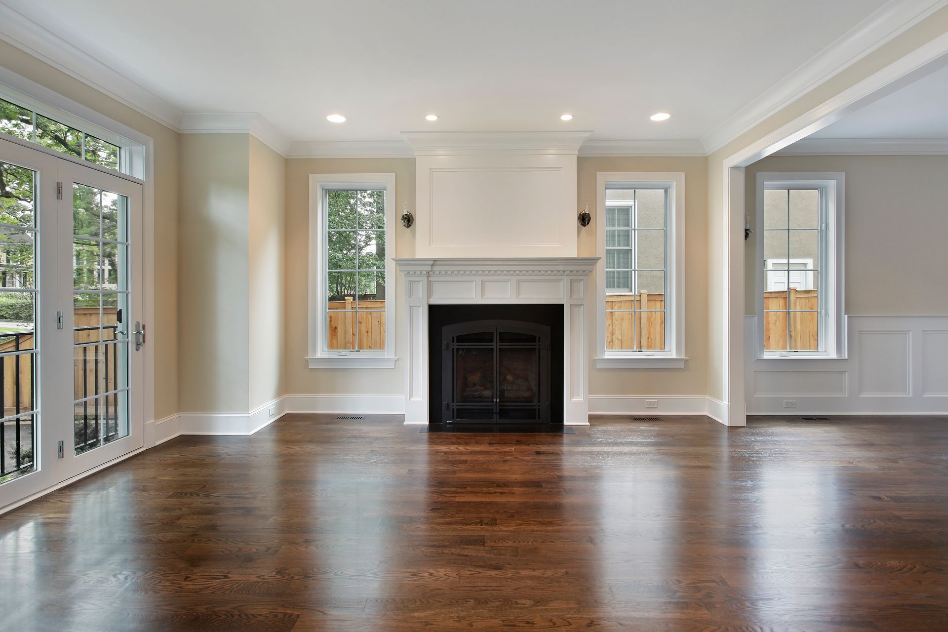 Empty living room with dark hardwood floors, white trim, a central fireplace, and multiple windows.