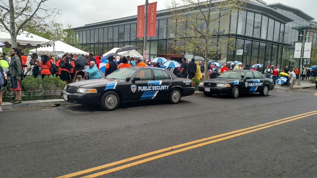 Two police cars are parked on the side of the road in front of a crowd of people.