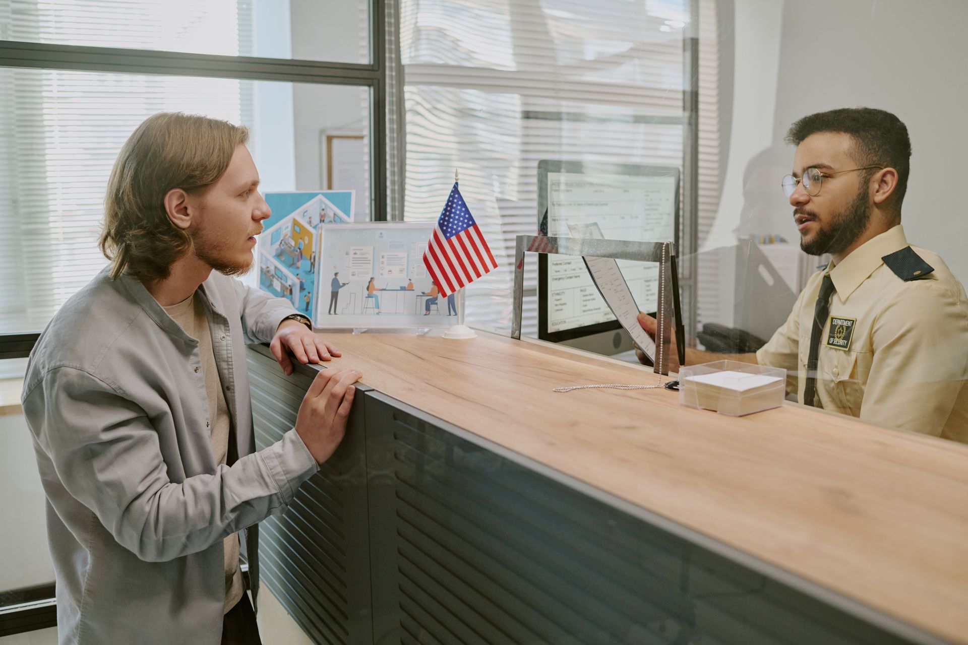 Front desk security officer assisting a visitor at a reception desk with protective glass.