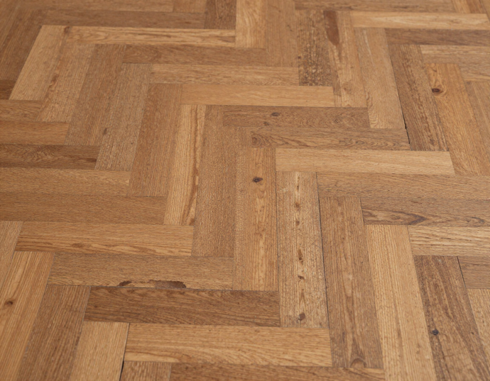 Primo piano di un pavimento in legno marrone  chiaro con motivo a spina di pesce.