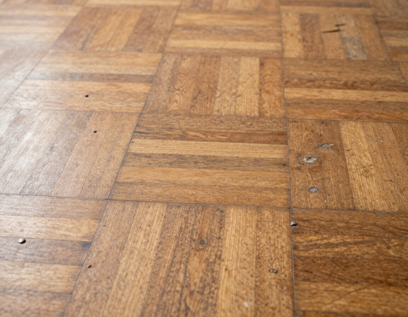 Primo piano di un pavimento in parquet di legno usurato, con graffi e segni di chiodi ben visibili