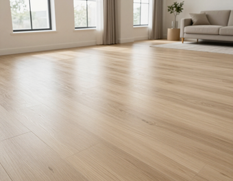 Soggiorno vuoto e luminoso, con pavimenti in legno chiaro, grandi finestre, tende e un divano beige in un angolo