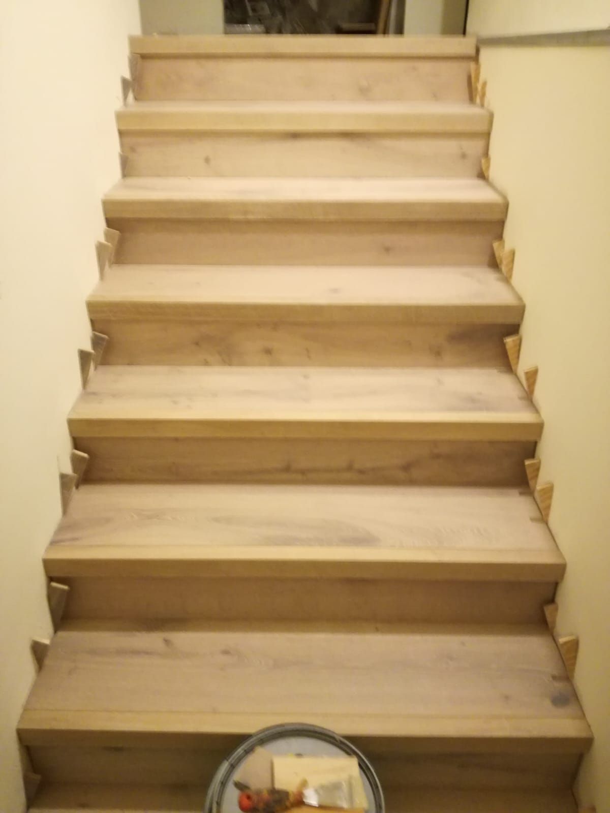 Scala in legno con gradini non rifiniti, vista dal basso all’interno di una casa.