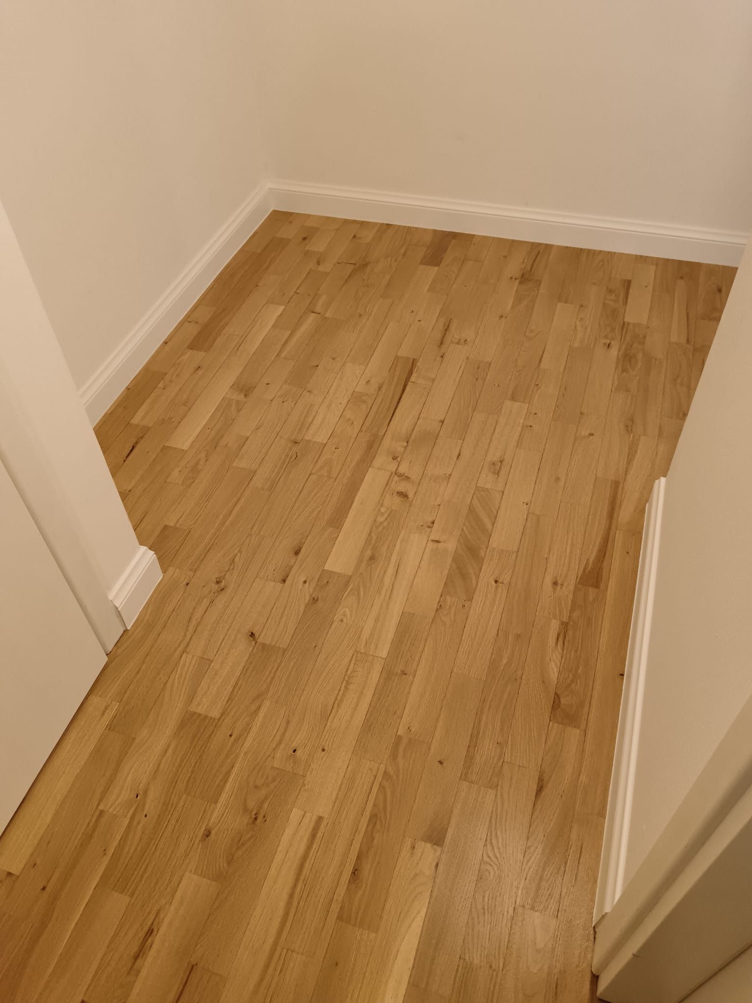 Piccola stanza vuota con pavimento in legno chiaro e pareti bianche, vista dalla porta