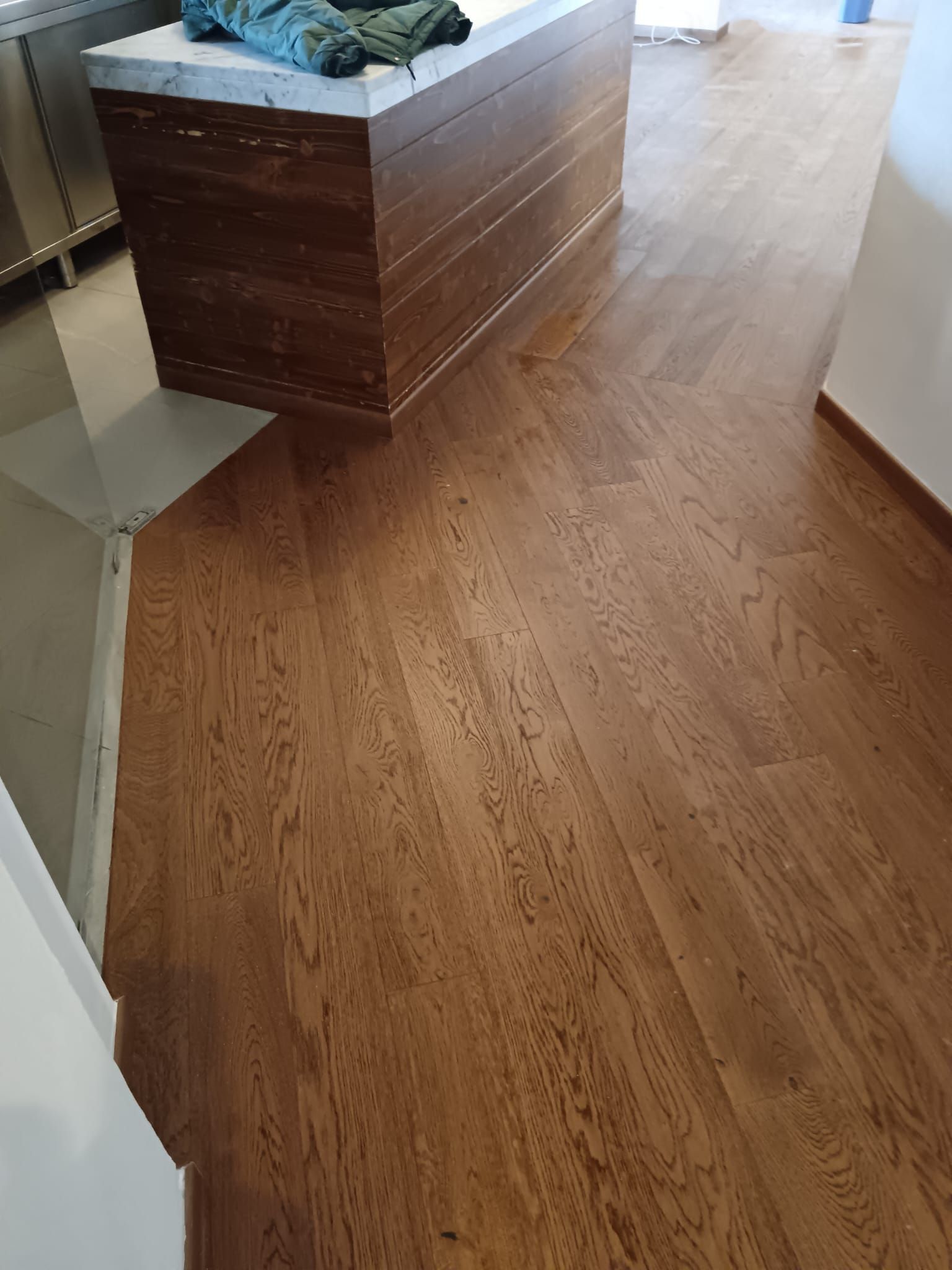 Isola da cucina in legno con piano blu, su un pavimento in legno chiaro in un ambiente simile a un corridoio.
