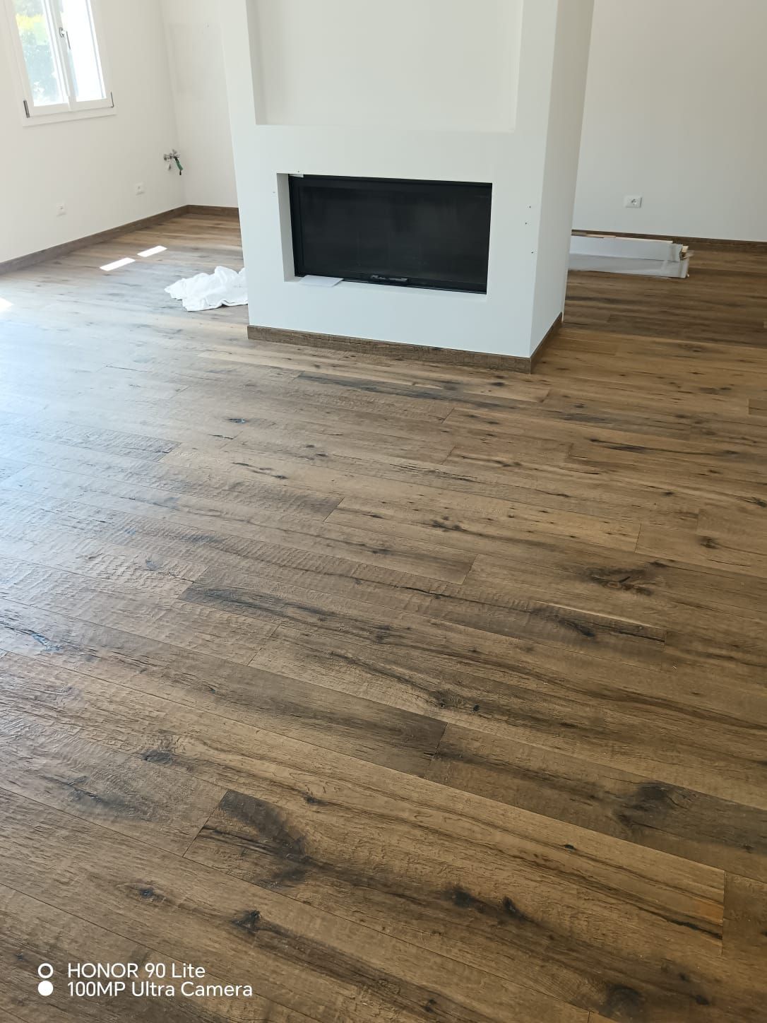 Stanza vuota con pavimento in legno e un inserto per camino nero incassato in una nicchia nella parete bianca