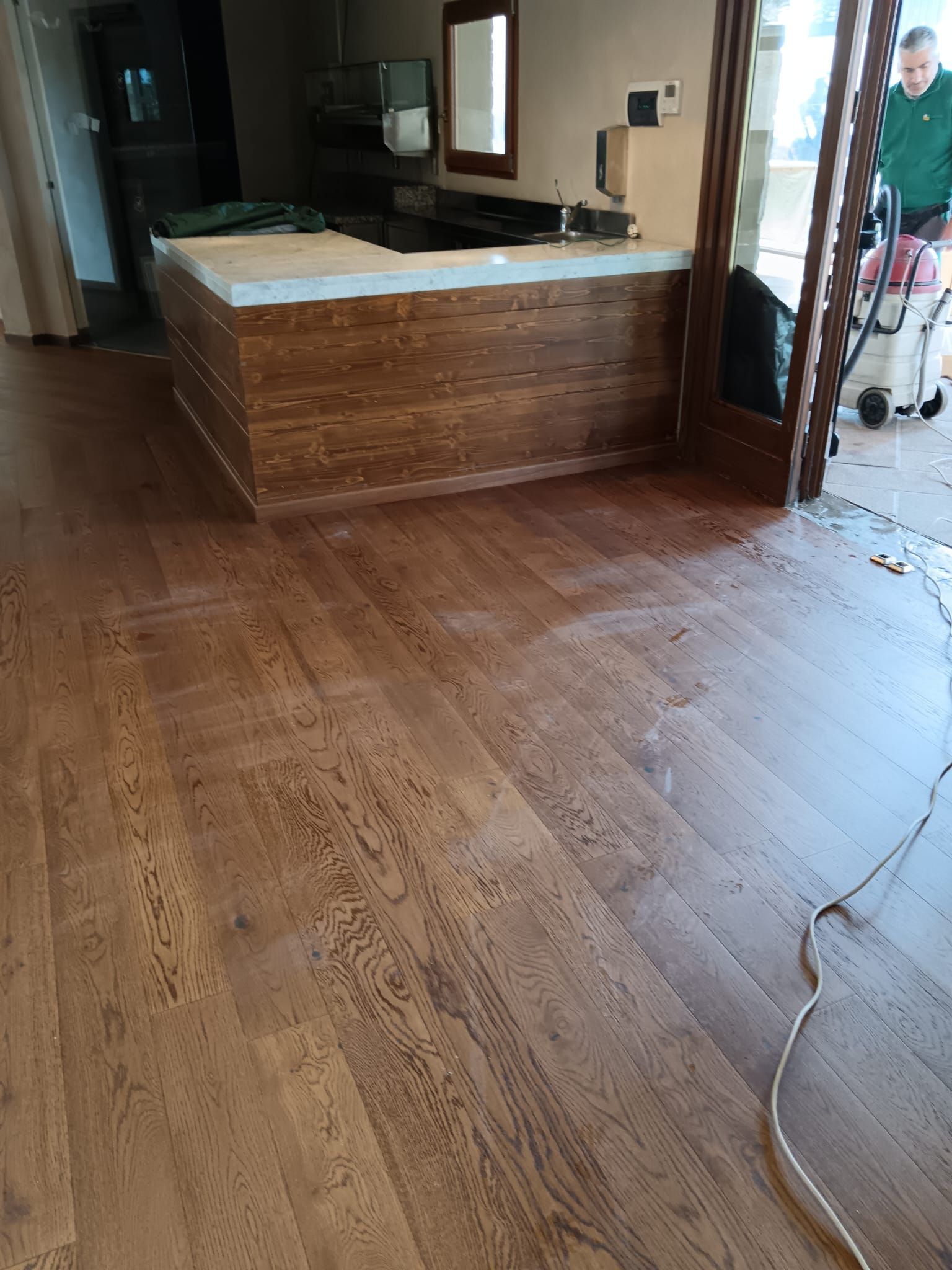 Stanza vuota con pavimento in legno e un piano di lavoro marrone, con un cavo di alimentazione sul pavimento vicino alla porta.