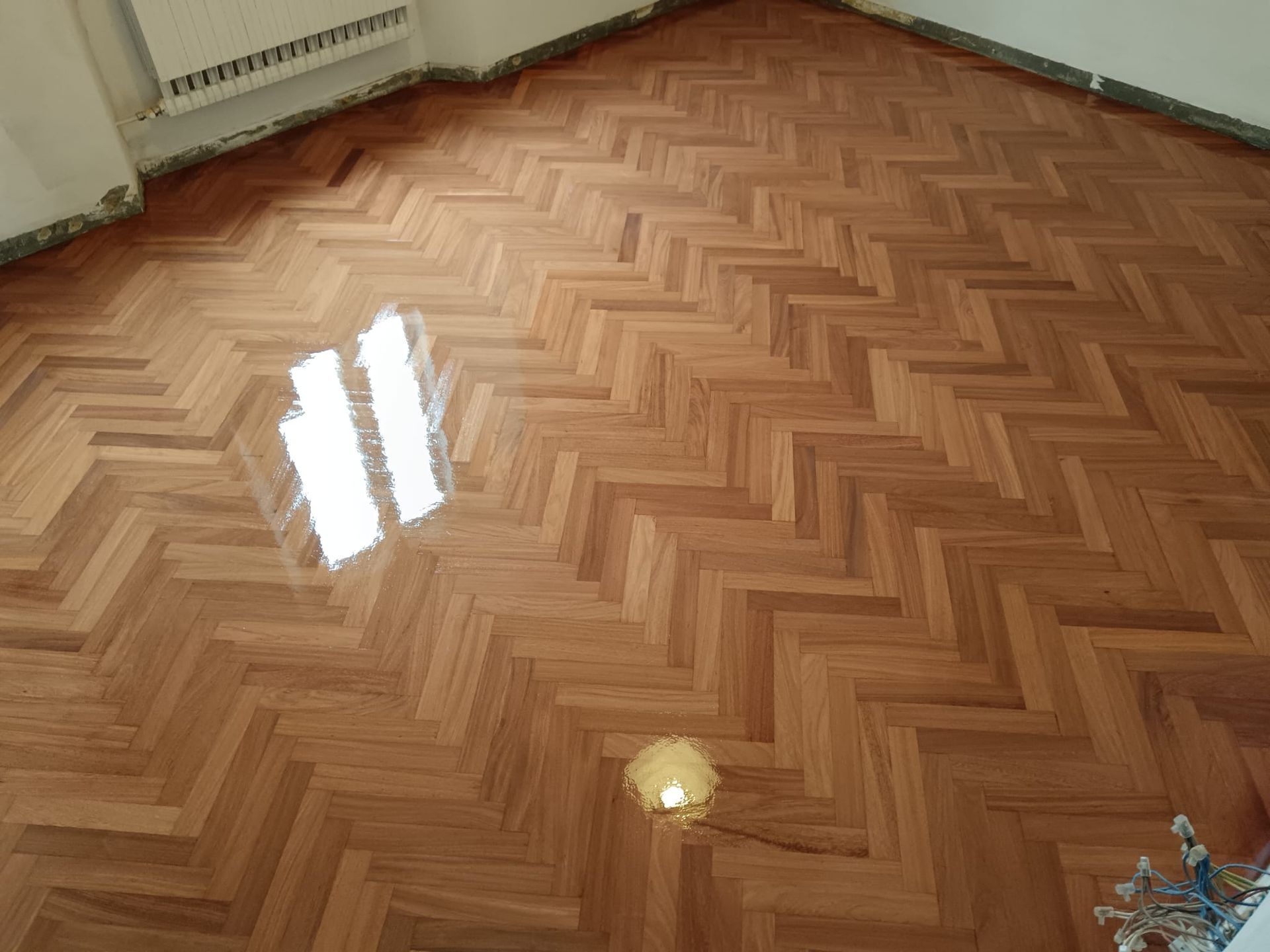 Pavimento vuoto in legno a spina di pesce, con il riflesso di una finestra luminosa e un piccolo giocattolo in un angolo