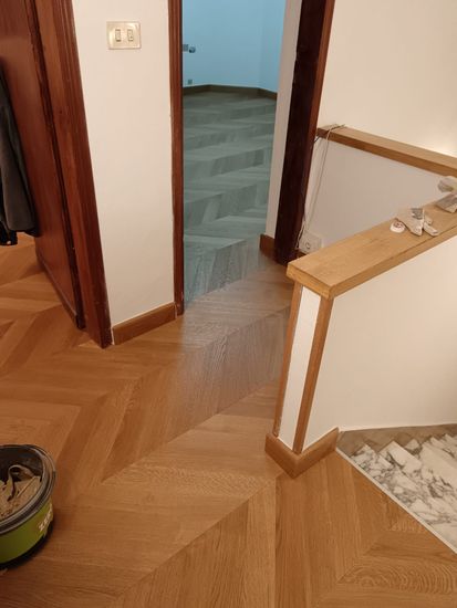 Corridoio con pavimento in legno, porta aperta e un robot aspirapolvere vicino all’angolo in basso a sinistra