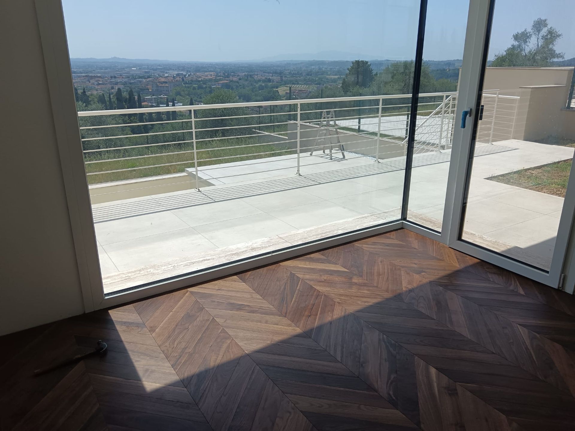 Stanza inondata di luce, con pavimento in legno a spina di pesce e porte a vetri che si aprono su un patio con vista panoramica