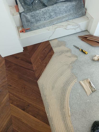 Moquette posata solo in parte accanto a una scala bianca, con attrezzi e materiali su un pavimento in legno.