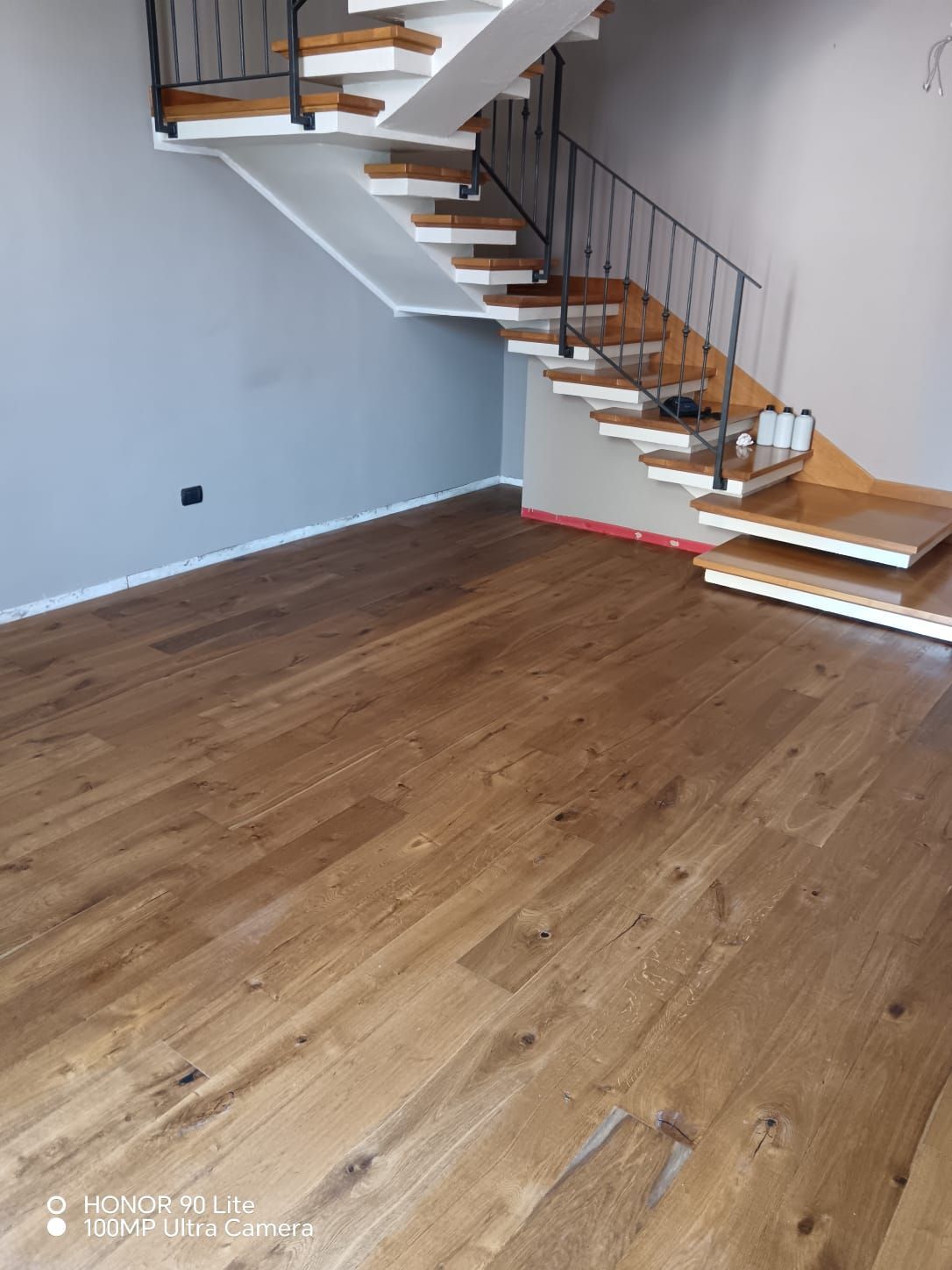 Stanza vuota con pavimento in legno, pareti bianche e una moderna scala con ringhiera in metallo.