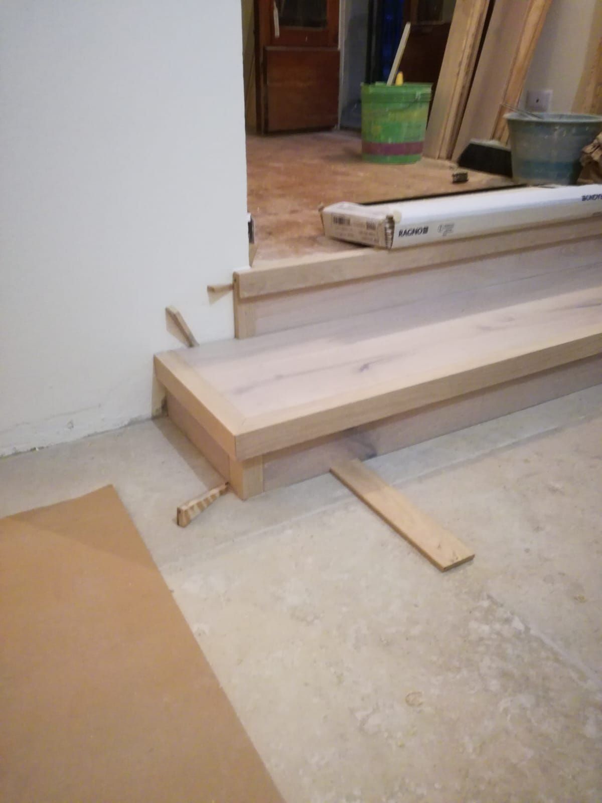 Rampa di legno in costruzione davanti a una porta, con assi e attrezzi su un pavimento di cemento.