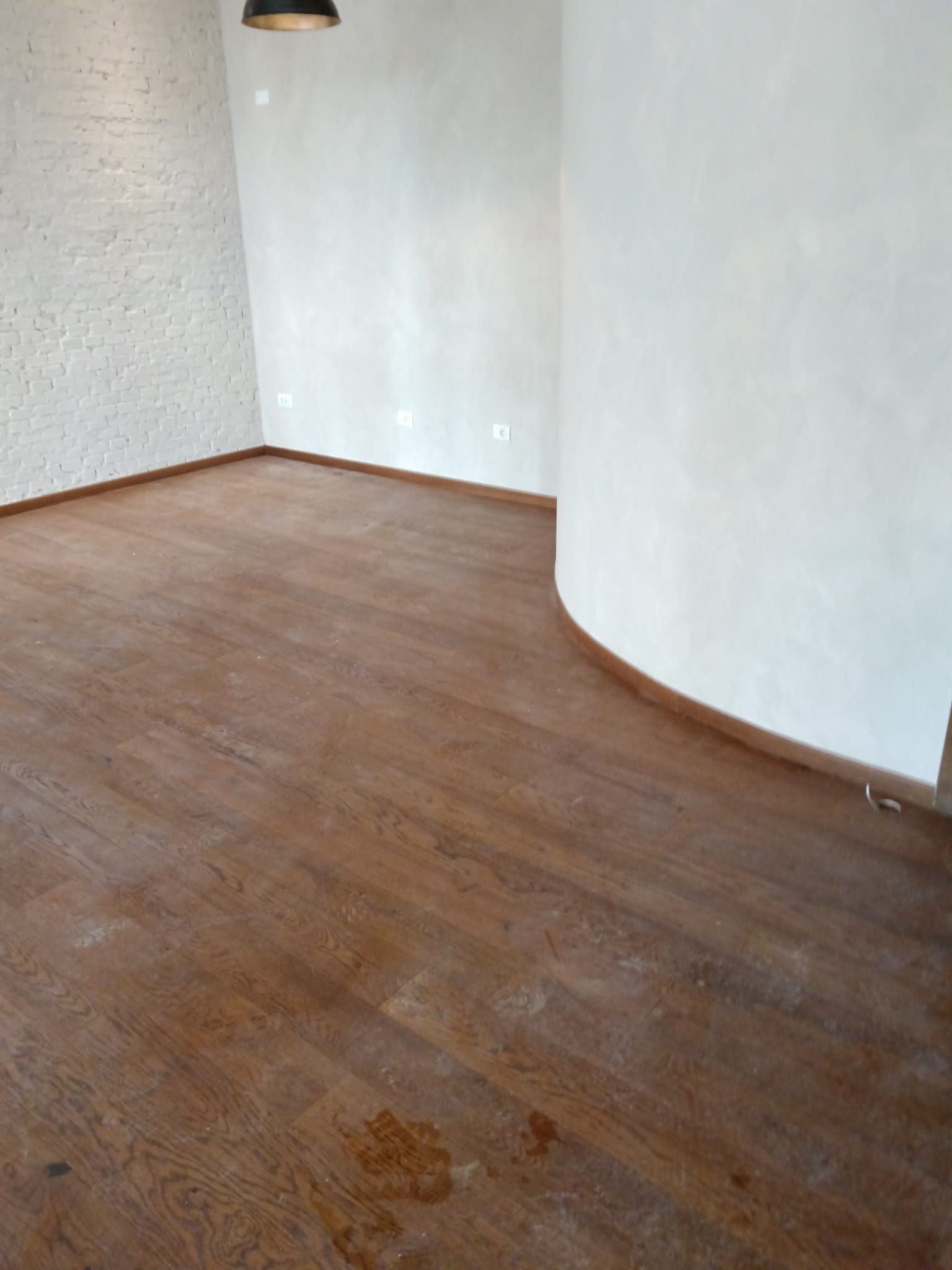 Stanza vuota con pavimento in legno marrone, pareti bianche e una sezione di parete curva