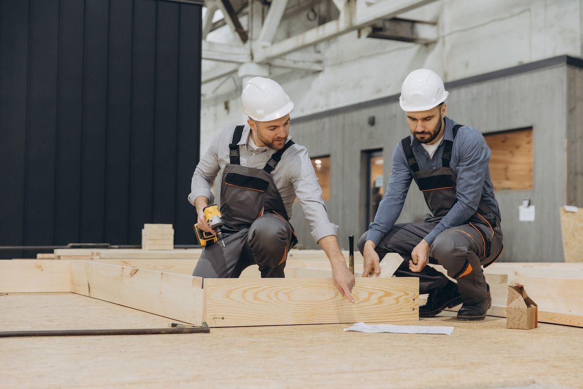 Two construction workers in hard hats measuring wooden panels at a building site