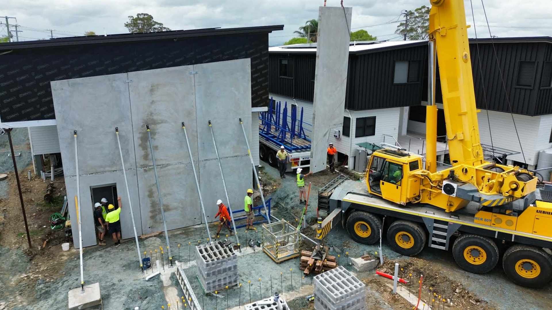 Construction site with a large yellow crane lifting a concrete wall. Workers in hard hats and a truck present — Crane Rentals in Taree, NSW