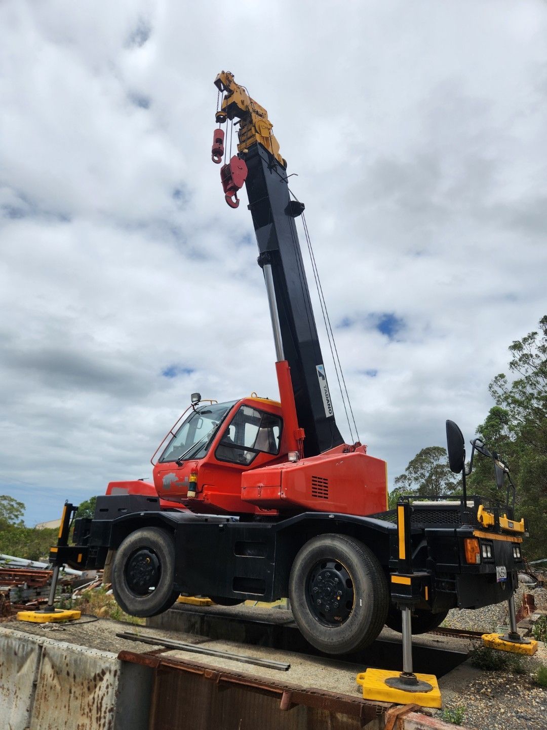 Red and black mobile crane with raised boom on a cloudy day — Crane Rentals in Taree, NSW
