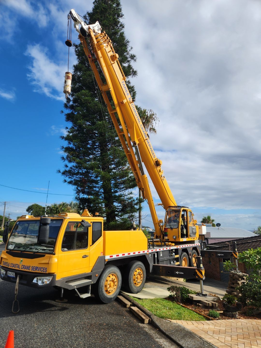 Yellow mobile crane extended, parked on a street near a house and trees — Crane Rentals in Taree, NSW