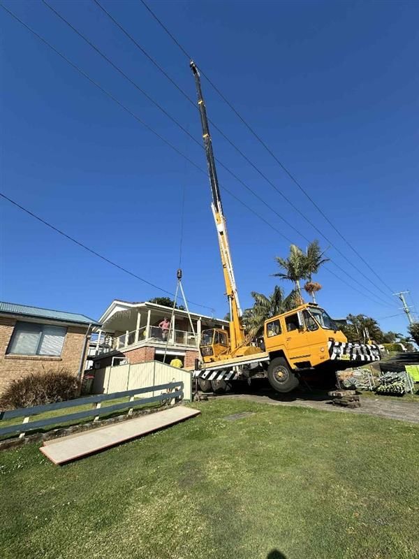 Yellow crane lifting near a house and power lines under a blue sky — Crane Rentals in Taree, NSW