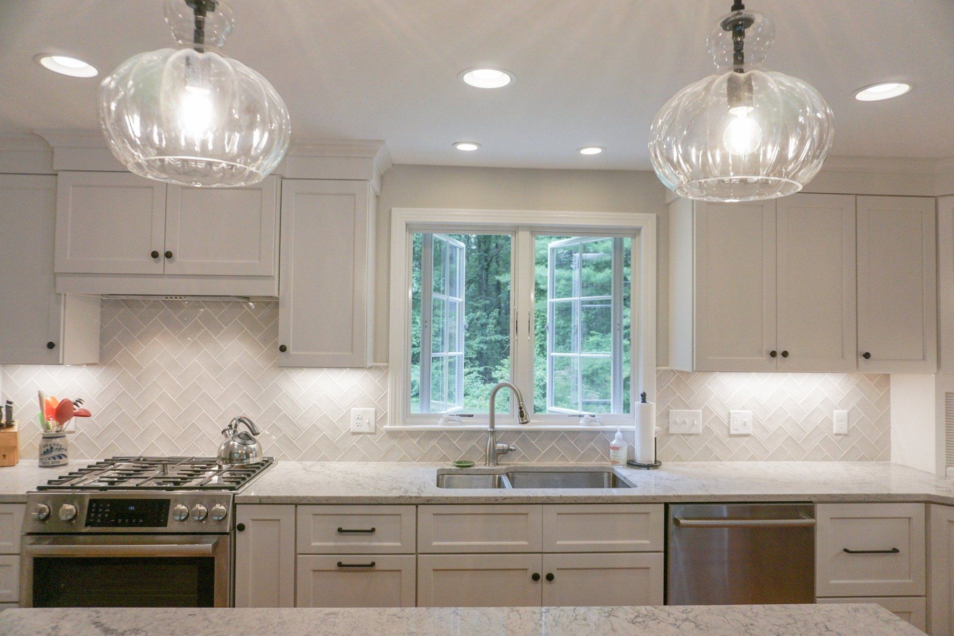 A kitchen with white cabinets , stainless steel appliances , a sink , and a window.